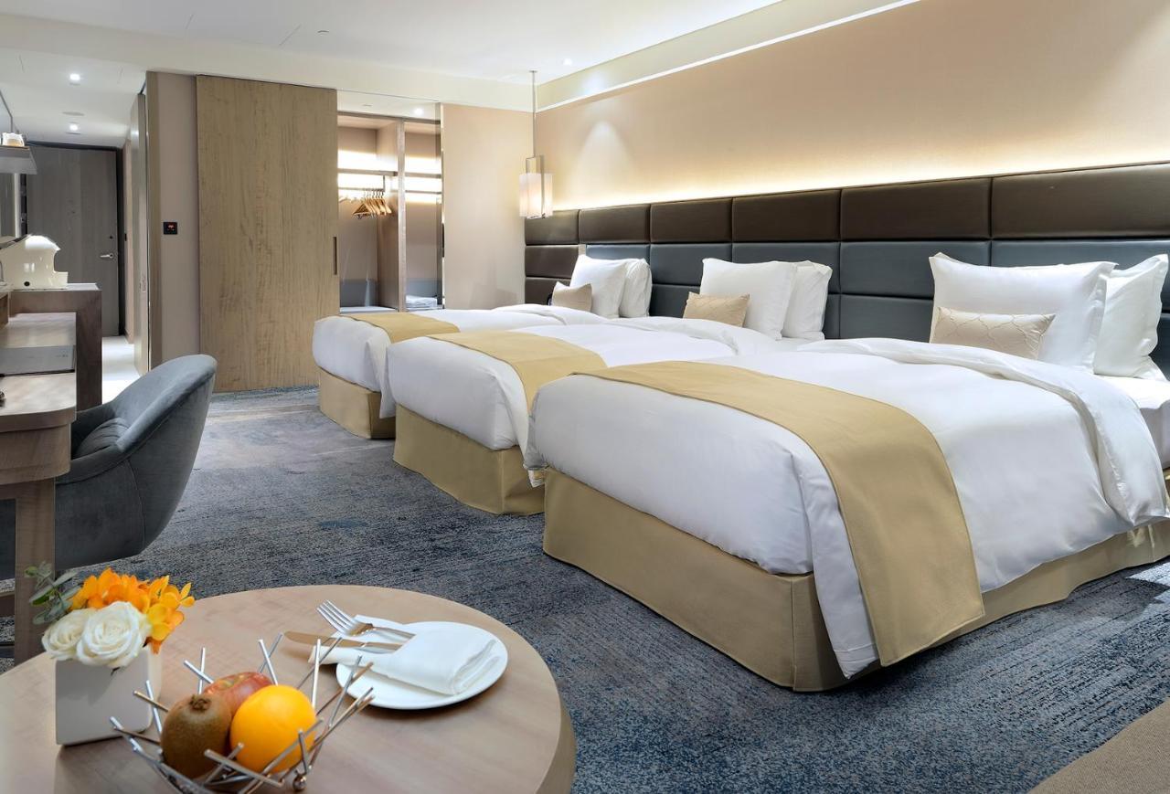 Caesar Park Hotel Banqiao Taipei Exterior photo The photo shows a modern hotel room featuring two beds with white linens and light beige accents. The walls are decorated in neutral tones, contributing to a spacious and airy feeling. There is a small table in the foreground that has a fruit display