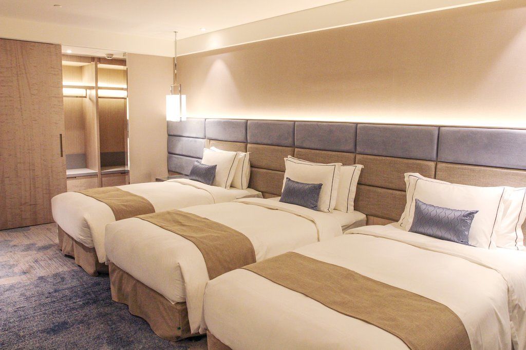 Caesar Park Hotel Banqiao Taipei Exterior photo The photo shows a modern hotel room with three neatly arranged beds. Each bed features a light-colored comforter with a tan stripe running down the center and a decorative pillow in a coordinating shade. The walls are a neutral color, and there is a 