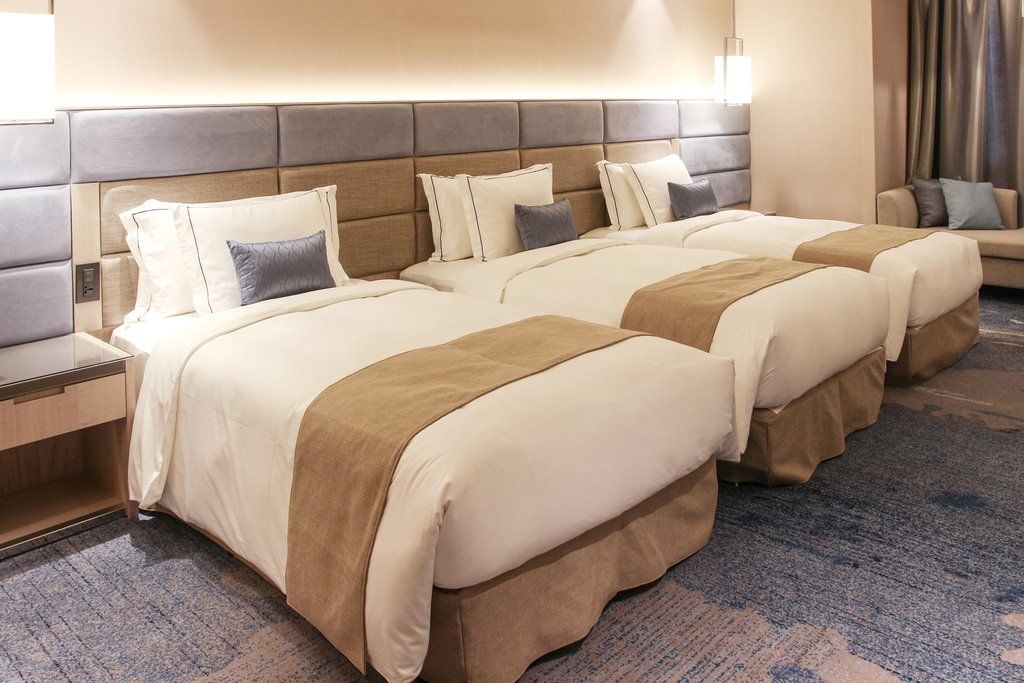 Caesar Park Hotel Banqiao Taipei Exterior photo The image shows a modern hotel room featuring three neatly made beds. Each bed has a cream-colored duvet and a beige throw blanket, along with decorative pillows. The headboard is upholstered in a combination of gray and beige tones. The room has sof