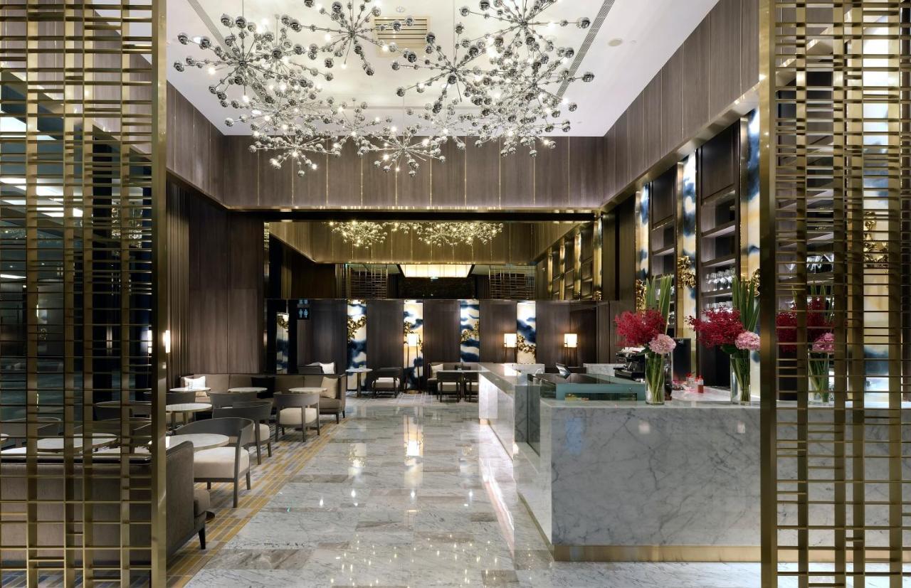 Caesar Park Hotel Banqiao Taipei Exterior photo The photo shows an elegant and modern hotel lobby. The space features luxurious decor with marble flooring and a tasteful color palette. The ceiling is adorned with stylish light fixtures that resemble abstract flowers or stars, creating a glamorous 