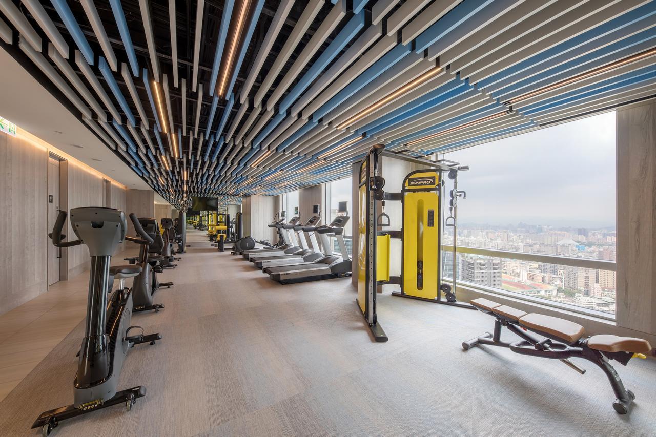 Caesar Park Hotel Banqiao Taipei Exterior photo The photo shows a modern gym environment with a sleek design. There are several pieces of exercise equipment, including treadmills and a weight training machine. The gym features a spacious layout with large windows that provide a view of the city ou