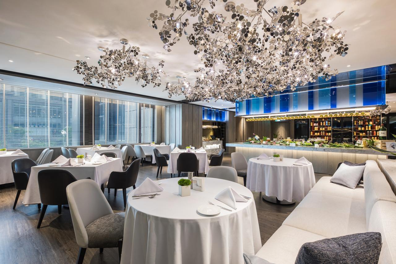 Caesar Park Hotel Banqiao Taipei Exterior photo The photo shows an elegant restaurant interior. The space features several round tables with white tablecloths, neatly set with dishes and napkins. 

A striking chandelier made of intricate, floral-like designs hangs from the ceiling, adding a modern