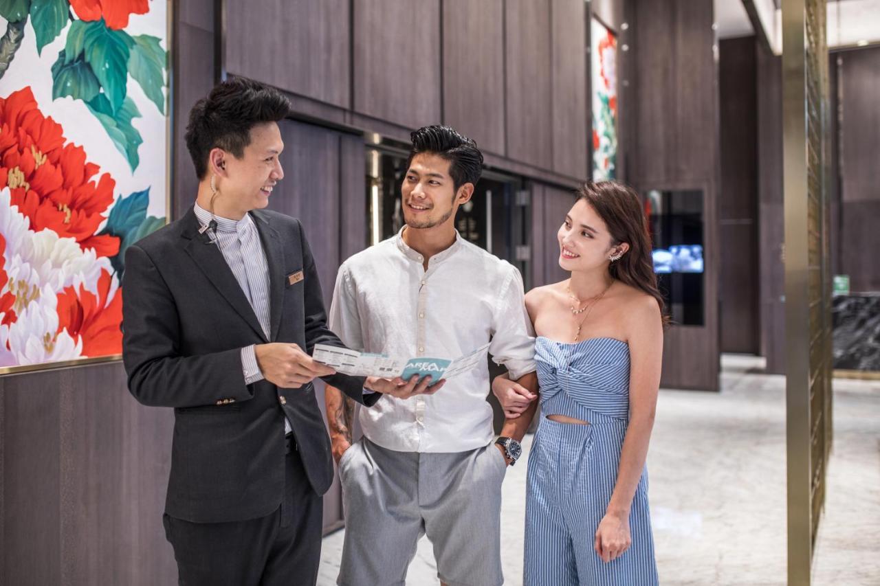Caesar Park Hotel Banqiao Taipei Exterior photo The photo shows three individuals interacting in a modern, upscale setting. One person, dressed in formal attire, appears to be providing information or assistance, possibly in a hospitality context. The other two individuals, a man and a woman, are 